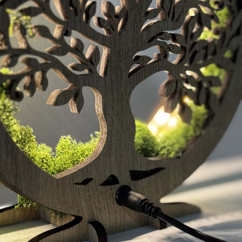 Detailní pohled na podsvícený dřevěný Strom života obklopený mechem.